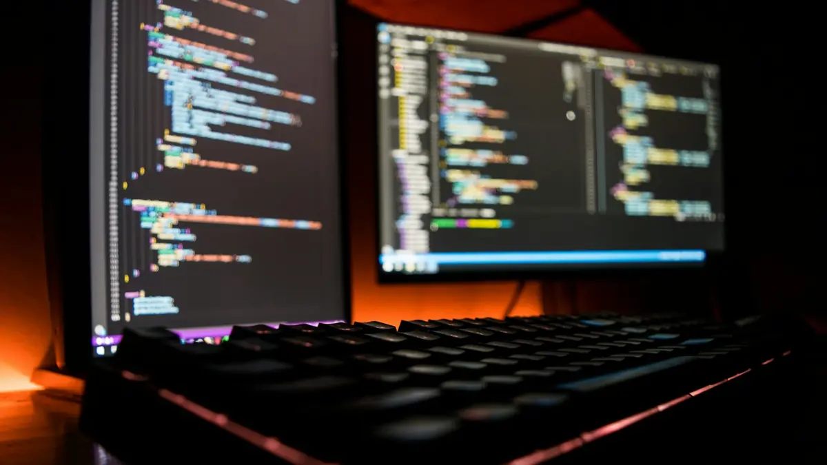 Mechanical keyboard in front of monitors showing code in a dark room